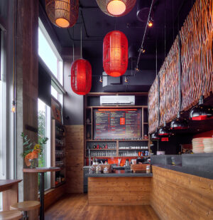 Le café moderne dispose dun intérieur en bois et dun haut plafond, avec des lanternes rouges mettant en valeur laménagement commercial. De grandes fenêtres invitent la lumière naturelle, tandis quun panneau de menu au-dessus du comptoir à café complète limage de marque. Des tables et des tabourets en bois confortables près de la fenêtre attendent les clients à la recherche dune expérience client unique.