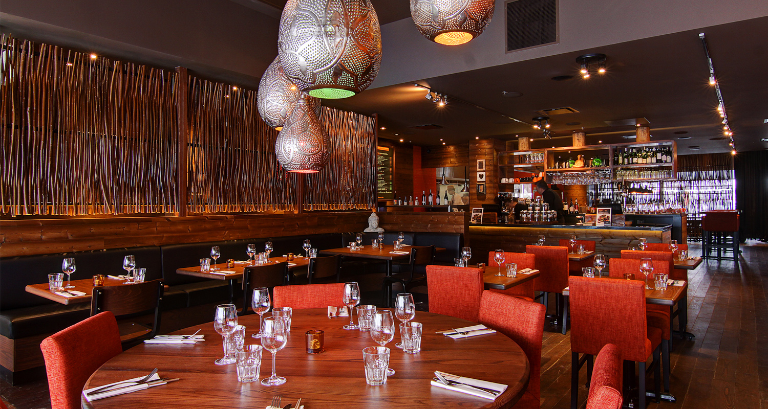 Le restaurant chaleureux est doté dun aménagement bien pensé, avec des murs en briques orange chaleureux. Des suspensions lumineuses projettent une douce lueur sur les tables dressées avec des verres et des couverts. Un grand miroir décoratif renforce la profondeur, tandis que les chaises rouges complètent à merveille les tons terreux.