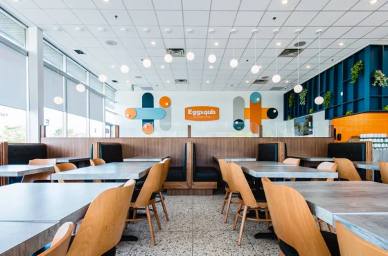 Modern, brightly lit design-commercial-restaurant with wooden tables, black booth seating, and decorative wall art featuring the word "Eggsquis" a space that truly reflects its image de marque.