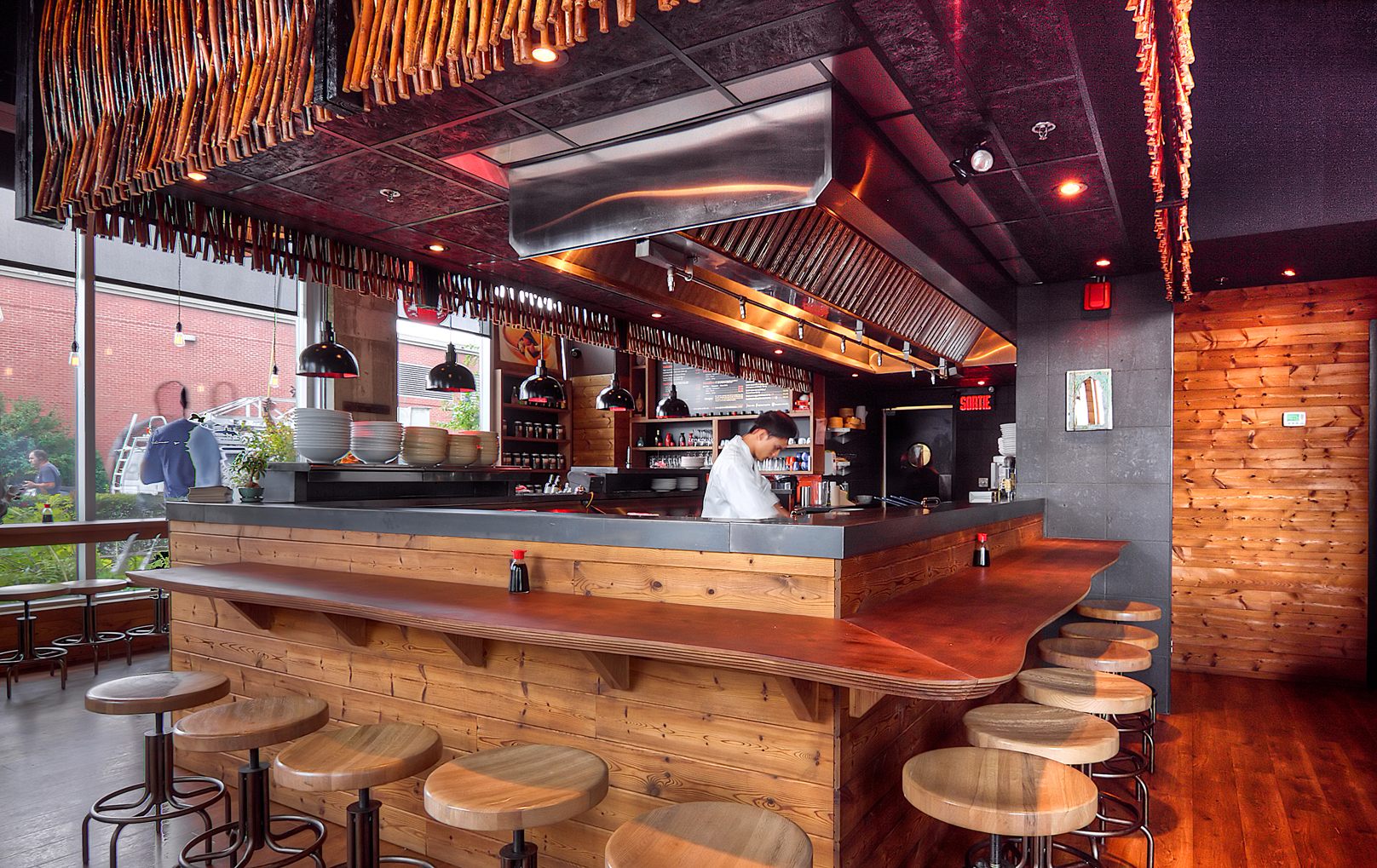 Design de cuisine ouverte par Dany Perron pour le restaurant Sésame : comptoir en bois massif, tabourets industriels, plafond architectural rouge et ambiance bistro asiatique à Montréal